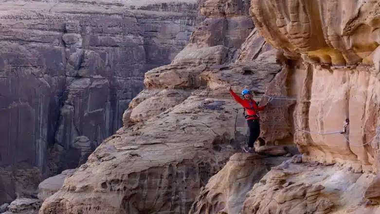 Participant scaling the Via Ferrata trail at AlUla Adventure Hub, embracing adventure against the backdrop of Saudi Arabian desert cliffs.