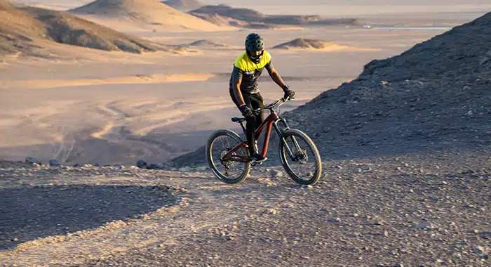 Cyclist riding along a desert trail at Alula Bike Park, with breathtaking rock formations and vast desert landscape.