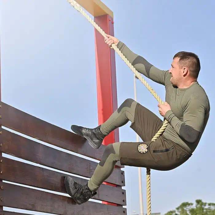 SWAT team participant climbing a rope over a high wall during the UAE SWAT Challenge, demonstrating strength and determination