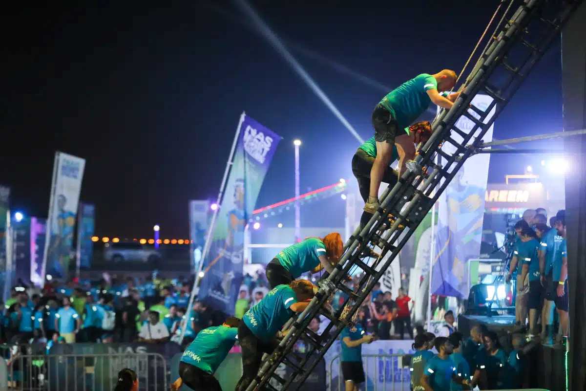 Competitor scaling a vertical obstacle at the NAS Night Challenge, illuminated with dynamic lights for a thrilling night-time race.