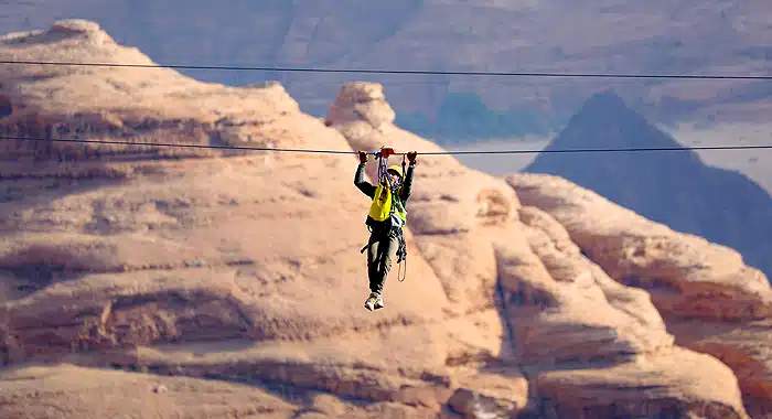 Adventurer riding the zipline at AlUla Adventure Hub, gliding over the scenic Saudi Arabian desert landscape