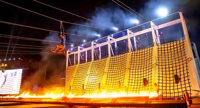 Participant gliding on a zipline above a fiery obstacle during the Government Games at Kite Beach, Dubai, showcasing courage and precision