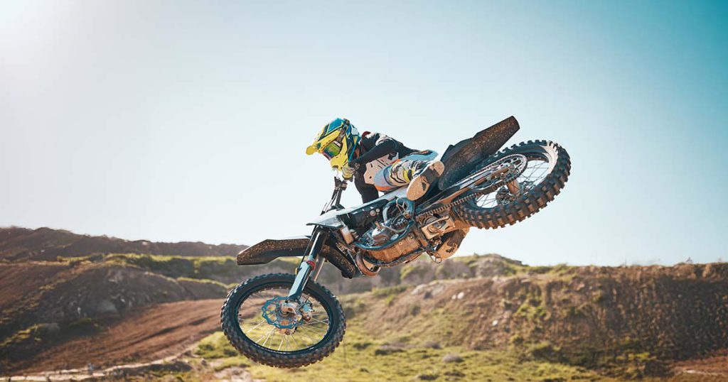 A motocross rider speeding on an off-road dirt bike through a sandy desert trail, conquering rugged terrain