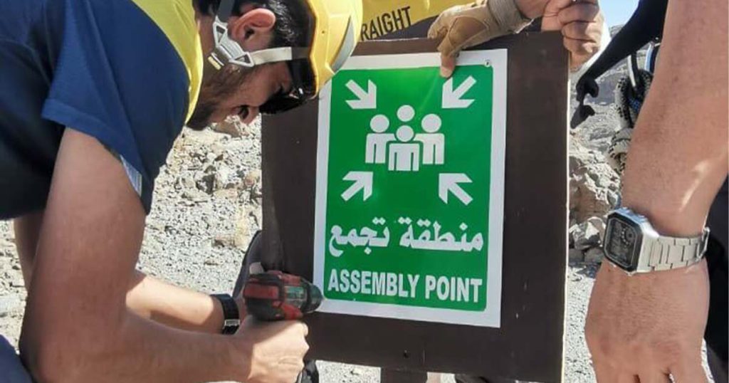 Worker installing an assembly point sign at an adventure park to guide visitors during emergencies.