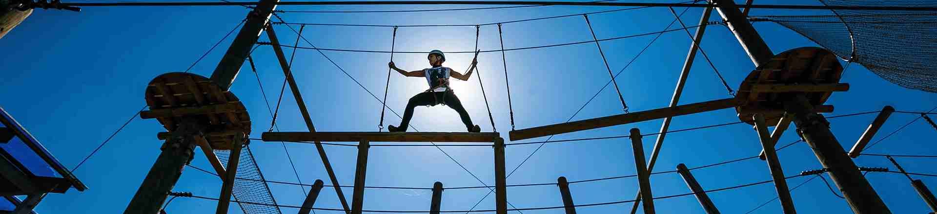 Child navigating a challenging high-ground obstacle course, hanging with ropes, and showcasing courage and balance in an adventure activity.